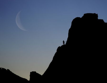A silhouette of a rock climber on the edge of the cliff. The size difference between climber and cliff is vast. This could represent struggle or overcoming fears.の写真素材