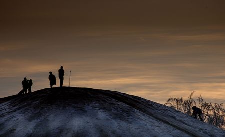 A snow-covered hill with late-night sledders silhouetted against a sunset.の写真素材