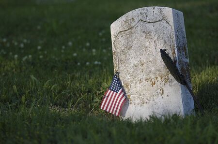 Gravestone with American flag in a field of grass and flowers. Space on headstone to insert any text or name.の写真素材