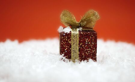 A red christmas present in fake snow against a red background.の写真素材