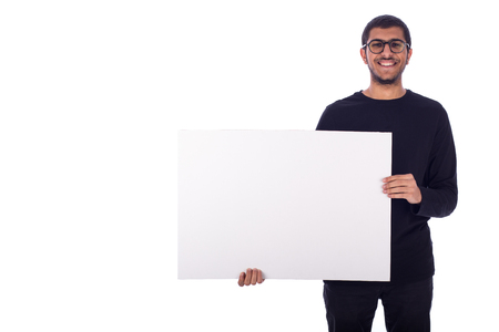 Happy friendly young man smiling and holding a blank board, guy wearing dark blue t-shirt and jeans, isolated on white backgroundの写真素材