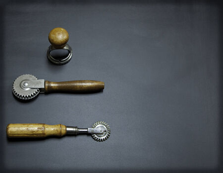 Antique pasta making tools on a black chalkboard background; pastry sealer, pasta cutter, and ravioli stamp; possible magazine layout; copy space on right sideの写真素材
