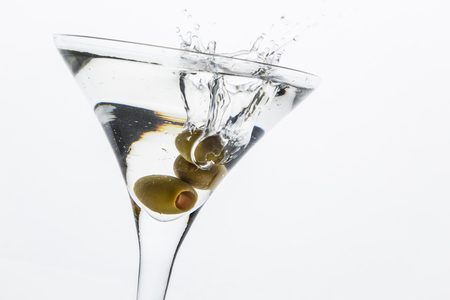 A martini glass on a white background; the water ripples and splashed as a green spanish olive with pimento is dropped into the glass; horizontal formatの写真素材