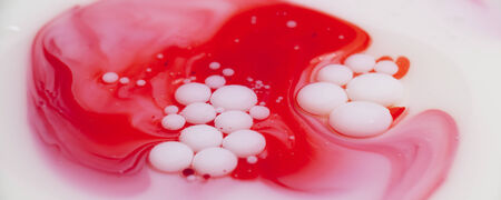 A layer of mineral oil on top of milk with milk bubbles floating above the oil; food coloring addedの写真素材