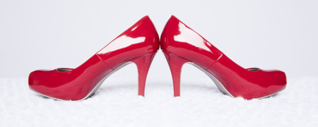A pair of sexy, red patent leather pumps sit atop a white fur surface with a white background; panoramic formatの写真素材