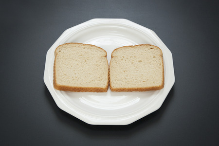 Two slices of white bread are side by side on a white plate; the first step in making a peanut...