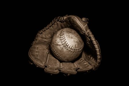 A worn softball sits inside an old baseball glove on a solid black background.  Image was lit by using a lightpainting technique.の写真素材