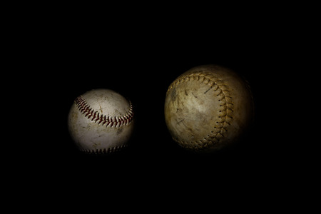 A worn softball and baseball sit alone on a solid black background.  This image was lit with a lightpainting techniqueの写真素材