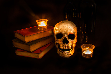 A vintage skull sits beside a stack of old novels and wine bottles; image created with a light painting techniqueの写真素材