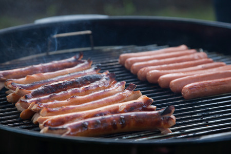 Multiple hot dogs sit cooking on a smoking charcoal grillの写真素材