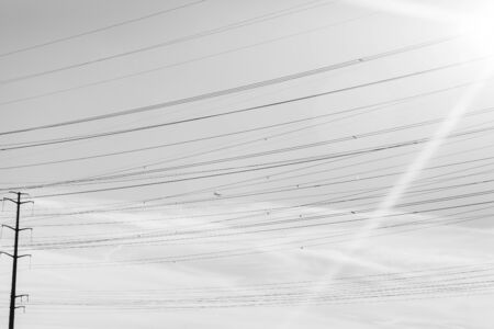 Power lines form an abstract image in black and white. This minimalistic look has a tiny airplane if you look closely.の写真素材