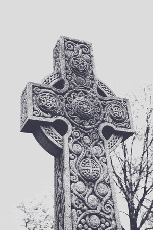 A Celtic cross tombstone with ornate details in an old cemetery.の写真素材