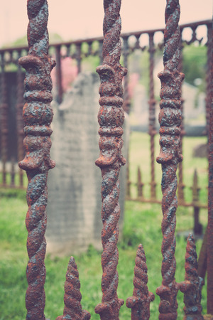 An old tombstone sits behind a rusty iron fence in a cemetery.の写真素材