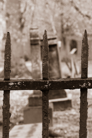Tombstones are seen beyond an old, rusty iron fence in a churchyard cemetery.の写真素材