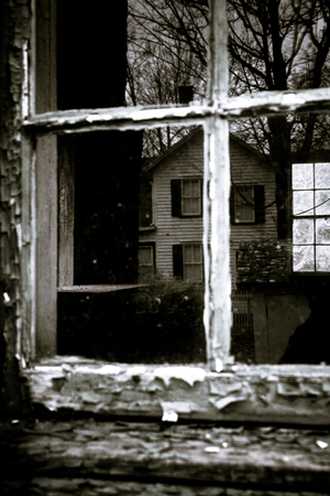 An old window reflects a colonial house. You can see straight through the house to the window on the other side.のeditorial素材
