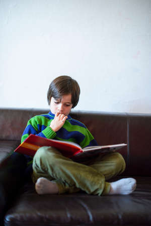child reads a book sitting on the couch