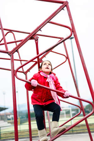 little girl climbs on iron frame of a basketball hoop in an outdoor basketball court