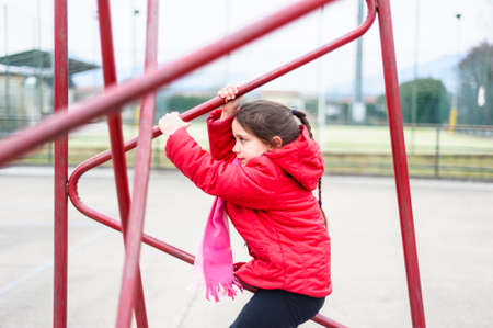 Little girl climbs on iron frame of a basketball hoop in an outdoor basketball court
