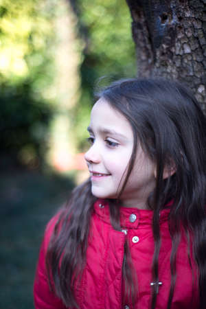 portrait of 7 year old girl in outdoor in the garden in winter with red jacket