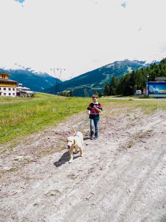 Child holds his golden retriever dog on a leash in a mountain meadow during a vacation and walkのeditorial素材