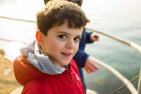 portrait of 9 year old boy with red jacket outside, as a lake backgroundの写真素材
