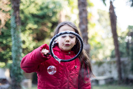 7 year old girl in outdoor in the garden in winter makes big soap bubbles