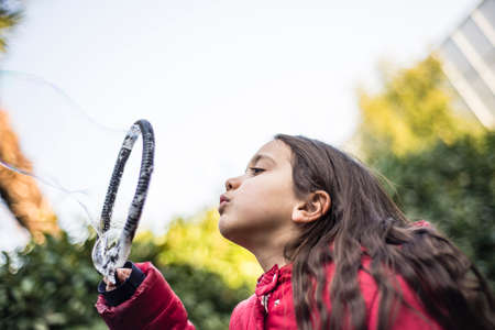 7 year old girl in outdoor in the garden in winter makes big soap bubblesの写真素材