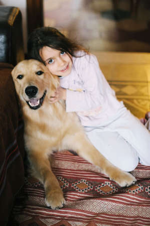 little girl at home with her golden retriever dog have affectionate gesturesの写真素材
