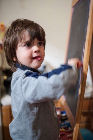 5-year-old boy writes on a blackboard in his home