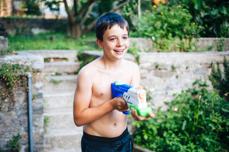 portrait of 13 year old boy in summer while playing with water guns in the home gardenの写真素材