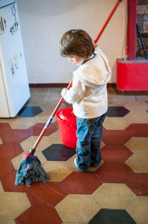 5-year-old boy washes the kitchen floor with the bucket and the ragの写真素材