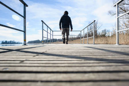 Lake Varese, Biandronno, Lombardy, Italy,man walks over a wooden pier and iron seen from behindの写真素材