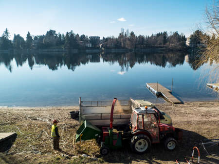 in a winter day worker at work along the river Ticino in Sesto calende Italy, tractor and truck shredding woodのeditorial素材