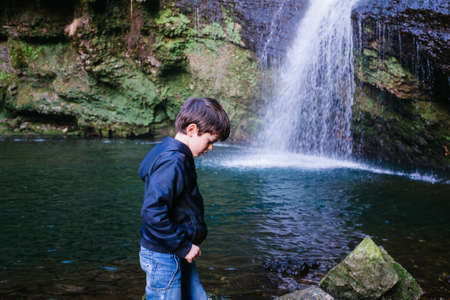 child portrait in front of a waterfall and a lagoon in the woodsの写真素材