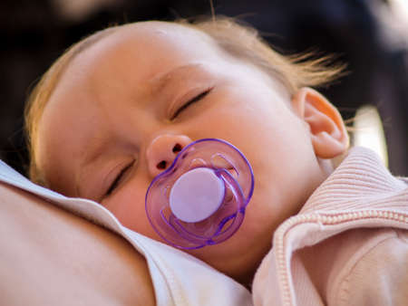 1 year old girl sleeps with a pacifier resting on her mother's breastの写真素材