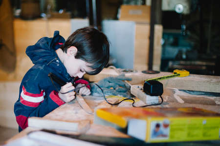 10-year-old boy in a carpenter's workshop learns to do small jobs, manual jobsの写真素材