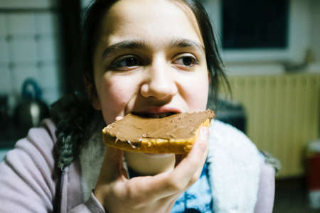teenage girl eats slice of bread with chocolate cream and hazelnuts for snack close up view