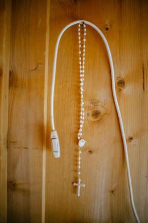 rosary wreath hanging from a nail on wooden wall together with the light switch wire