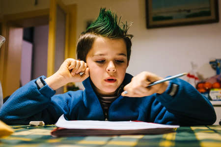 portrait of 9 year old boy at home with green colored hair crest performing school homework