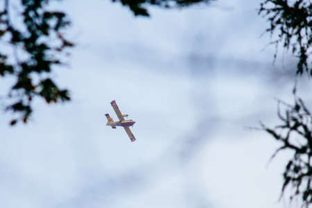 Canadair airplane flies over wood with much smoke caused by forest fire, fire fighting intervention