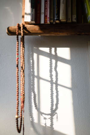 Buddhist rosary made of wooden beads is hung and illuminated by the sun produces shade on the wall