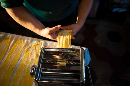 preparation of fresh egg pasta homemade noodles with the hand machine, on the kitchen table at home, rotating crankの写真素材