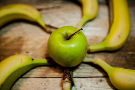 an apple in the middle with bananas around forming a wheel on rough wood backgroundの写真素材