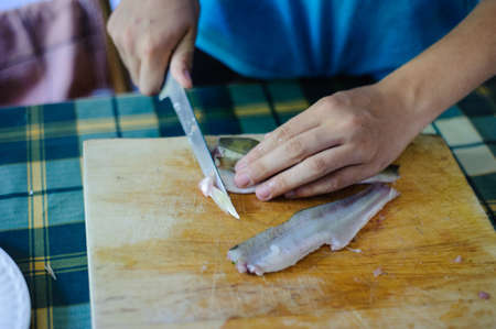 cook hands clean fish meat with knife on wooden chopping boardの写真素材