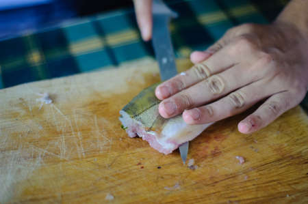 cook hands clean fish meat with knife on wooden chopping board