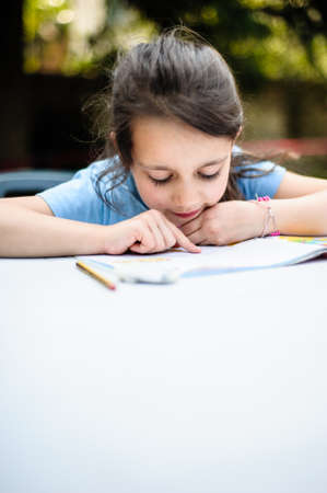 little girl at home reads and does school homework, remote lesson for isolation