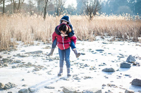 little girl carries her brother on the shoulder in the winter outdoors in the park
