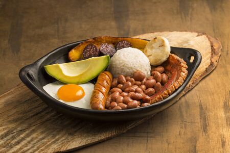 Tray paisa, typical dish at the Antioque? ? a region of Colombia. It consists of chicharrón (fried pork belly), black pudding, sausage, arepa, beans, fried plantain, avocado egg, and riceの写真素材