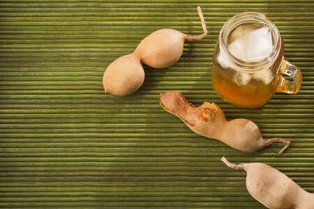 Tamarind juice in a glass surrounded by fresh ripe tamarinds - Tamarindus indicaの写真素材