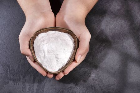 Female hands holding bowl of baking soda - wooden background